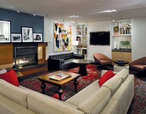The Den’s lounge in The Fifty Sonesta Select New York features armchairs and sofas, coffee tables and a fireplace, plus a large TV.