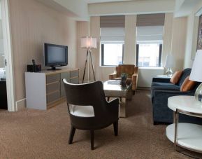 The Benjamin Royal Sonesta New York guest room, featuring chairs, sofa, coffee table, windows, and a television.