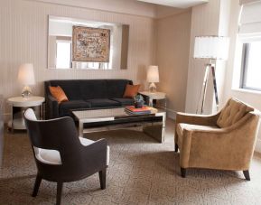 The Benjamin Royal Sonesta New York guest room living area, furnished with coffee table, chairs, TV, and sofa.
