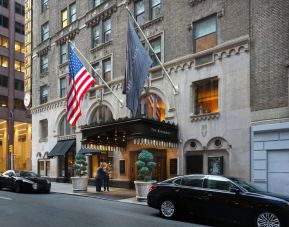 The Benjamin Royal Sonesta New York’s exterior features the hotel’s name on the awning and flag, with a Stars and Stripes flag beside it, and large potted plants.