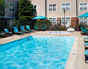 The outdoor pool at Sonesta ES Suites Chicago Waukegan Gurnee ha a nearby hot tub, shaded tables and chairs, and sun loungers and chairs by the side of the pool.