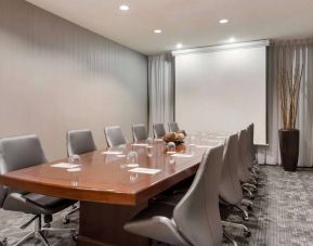 Sonesta Select Tempe Downtown meeting room, featuring long wooden table, a dozen swivel chairs, and a projector screen.