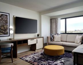 Sonesta Irvine guest room living area, including corner sofa, chair, window, and large, wall-mounted TV.