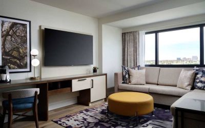 Sonesta Irvine guest room living area, including corner sofa, chair, window, and large, wall-mounted TV.