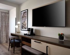 Sonesta Irvine guest room workspace, furnished with desk, chair, and lamp, plus a nearby widescreen TV.