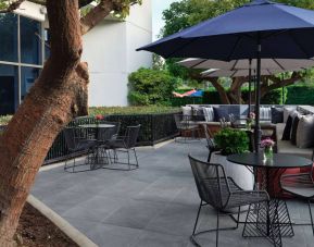 The patio at Sonesta Irvine features sofa seating alongside tables and chairs (shade available), with flowers on each table.