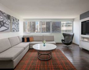 Royal Sonesta Chicago Downtown guest room lounge, with large sofa, chair, and coffee table, plus a wall-mounted TV.