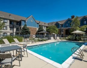 The hotel’s outdoor pool features tables and chairs, with shade available, and sun loungers by the side, with greenery beyond the fence.