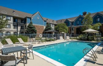 The hotel’s outdoor pool features tables and chairs, with shade available, and sun loungers by the side, with greenery beyond the fence.