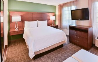 Double bed guest room in Sonesta ES Suites Fort Lauderdale Plantation, featuring bedside lamps, windows, and a large TV.