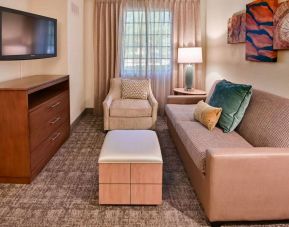 Sonesta ES Suites Fort Lauderdale Plantation guest room living area, furnished with sofa, armchair, window, and a widescreen television.