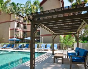 Sonesta ES Suites Fort Lauderdale Plantation’s outdoor pool has sofa seating and a coffee table by the side, alongside a row of sun loungers.