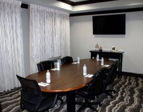 Hotel meeting room, including a wooden table and five leather chairs around it, two windows, and a large TV on the wall.