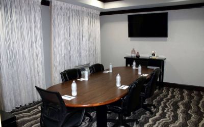 Hotel meeting room, including a wooden table and five leather chairs around it, two windows, and a large TV on the wall.