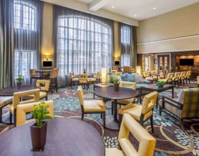 The hotel’s breakfast area has a carpeted floor, range of table sizes, seating from normal chairs to tall stools and armchairs, high ceilings and large windows, plus multiple TVs.