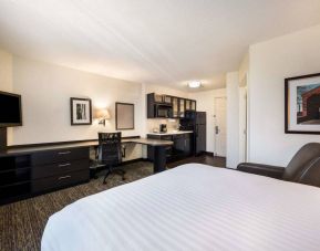 Sonesta Simply Suites Atlanta Gwinnett Place double bed guest room, with workspace desk and chair, kitchen, armchair, and a widescreen TV.