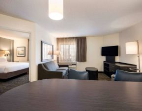 Double bed guest room in Sonesta Simply Suites Oklahoma City Airport, including a living area with sofa, TV, window, and a table and chairs.