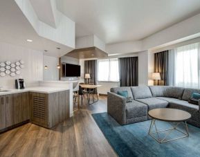 Guest room living area in Sonesta Columbus Downtown, including corner sofa and coffee table, large windows, and a TV with table and chairs nearby.