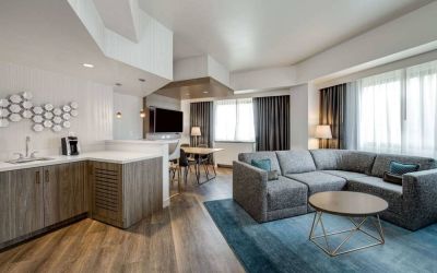 Guest room living area in Sonesta Columbus Downtown, including corner sofa and coffee table, large windows, and a TV with table and chairs nearby.