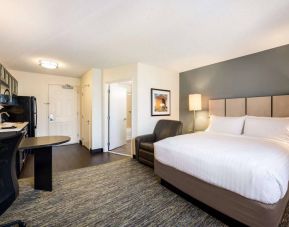 Double bed guest room in Sonesta Simply Suites Plano Frisco, furnished with kitchen, art on the wall, and an armchair.