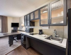 Sonesta Simply Suites Plano Frisco’s kitchen features a table and chair, microwave, hob, and fridge-freezer.