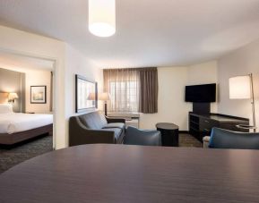 Sonesta Simply Suites Dallas Las Colinas double bed guest room, including sofa, window, and TV.