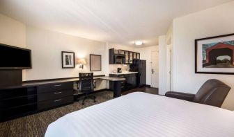 Sonesta Simply Suites Dallas Las Colinas double bed guest room, furnished with armchair, TV, and workspace desk and chair.