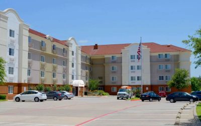 The hotel’s exterior has ample parking for guests, a US flag fluttering on a flagpole, and abundant greenery.