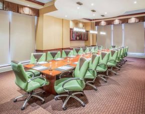 Hotel meeting room, furnished with a long wooden table and 18 green swivel chairs.