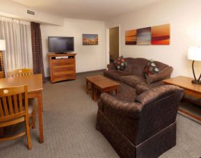 Sonesta ES Suites Dallas Las Colinas guest room living area, furnished with table and chairs, sofa, armchair, coffee tables, and TV.