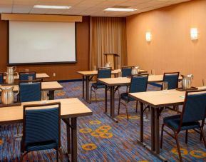 Hotel meeting room with seating for a dozen attendees and tables arranged in a classroom format facing a projector screen.