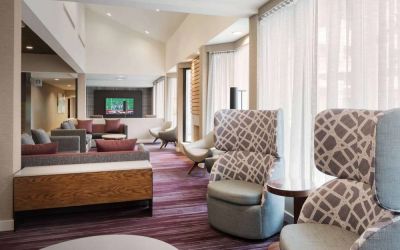 The lobby lounge at Sonesta Select Whippany Hanover features sofas and armchairs, coffee tables, large windows, and a large TV.
