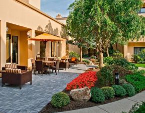 The hotel’s patio is furnished with a mix of tables and chairs, and sofa/armchair seating, next to flowerbeds and trees.