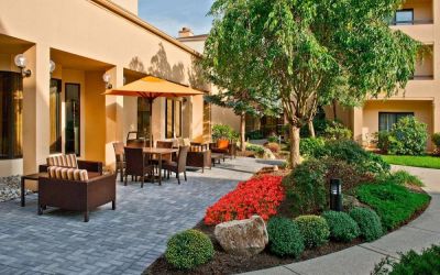 The hotel’s patio is furnished with a mix of tables and chairs, and sofa/armchair seating, next to flowerbeds and trees.