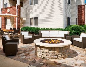 Sonesta ES Suites Annapolis’ patio features a fire pit surrounded by armchairs and a sofa, with a shaded table and chairs nearby.