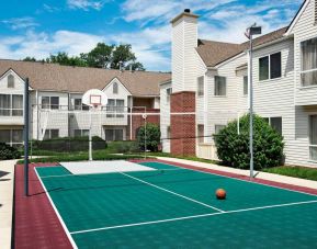 The hotel’s basketball court has a fence by the hoop, and is surrounded by hotel buildings and pleasant greenery.