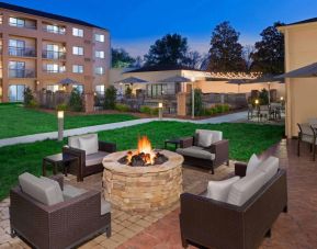 Sonesta Select Raleigh Durham Airport Morrisville’s fire pit has armchair and sofa seating, plus coffee tables, next to it, with shaded tables and chairs nearby.