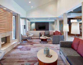 Sonesta Select Raleigh Durham Airport Morrisville’s lobby lounge is furnished with comfy chairs, coffee tables, and sofas, plus a fireplace and TV.
