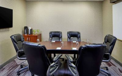 Hotel meeting room, with a wooden table surrounded by six leather chairs, a wall-mounted TV, and a whiteboard.