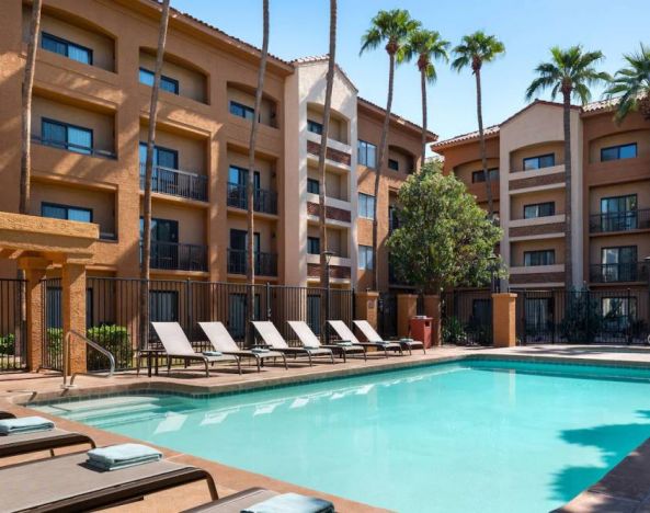 Sonesta Select Phoenix Camelback’s outdoor pool has sun loungers by the side, a shaded area, and tall palm trees.