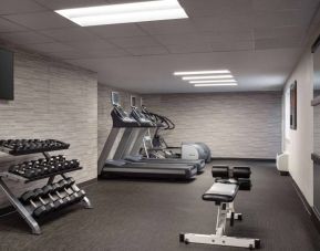 The fitness center at Sonesta Select Phoenix Camelback is equipped with free weights, a range of exercise machines, and a wall-mounted television.