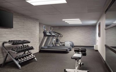 The fitness center at Sonesta Select Phoenix Camelback is equipped with free weights, a range of exercise machines, and a wall-mounted television.