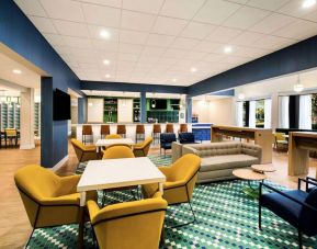 Sonesta Select Philadelphia Airport’s lobby lounge is furnished with tables and chairs, plus sofas and armchairs, and has a large, wall-mounted TV.