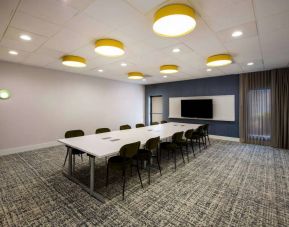 Hotel meeting room, with long table, a dozen chairs, spacious room, and a large TV mounted on the wall.