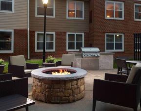 The fire pit at Sonesta ES Suites Raleigh Cary has armchairs around it, a barbecue, and potted plants.