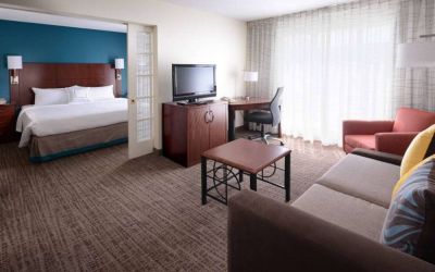 Double bed guest room in Sonesta ES Suites Dallas Medical Market Center, featuring a living area with sofa, armchair, and TV.