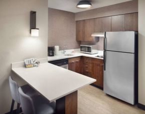Guest room kitchen in Sonesta ES Suites Raleigh Durham Airport Morrisville, featuring fridge-freezer, hob, microwave, and table.
