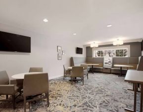 Lounge seating area, featuring tables and chairs, plus booth seating and a wall-mounted TV, at Sonesta ES Suites Reno.