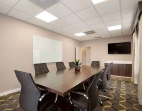 Hotel meeting room furnished with long wooden table, eight swivel chairs, a whiteboard, and a wall-mounted television.