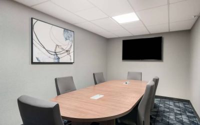 Hotel meeting room with wooden table, half a dozen chairs, and a wall-mounted television.